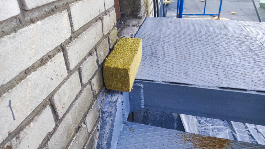 Обрезок минеральной ваты на металлической лестнице у кирпичной стены