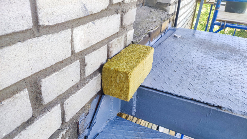 Угол кирпичной стены и минеральная вата на ступени металлической лестницы