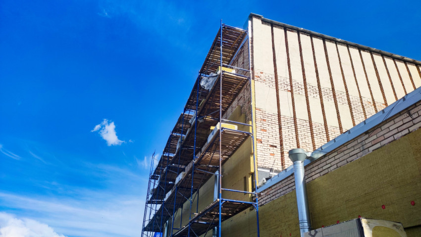 Многоярусные строительные леса у высокой кирпичной стены на фоне синего неба
