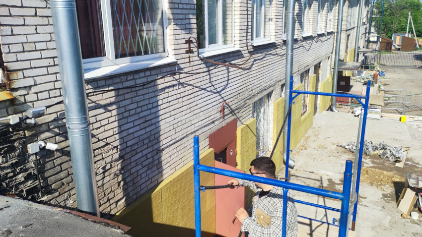 Рабочий на строительных лесах у кирпичного фасада с окнами и водостоками