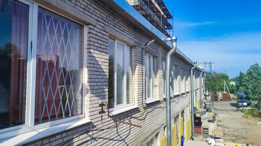 Кирпичный фасад с окнами, водосточными трубами и лесами под карнизом