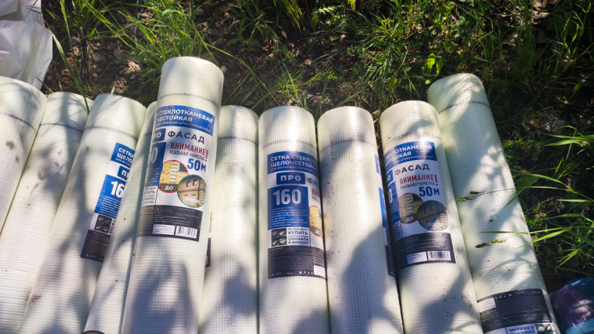 Рулоны стеклотканевой фасадной сетки на траве рядом со стройплощадкой