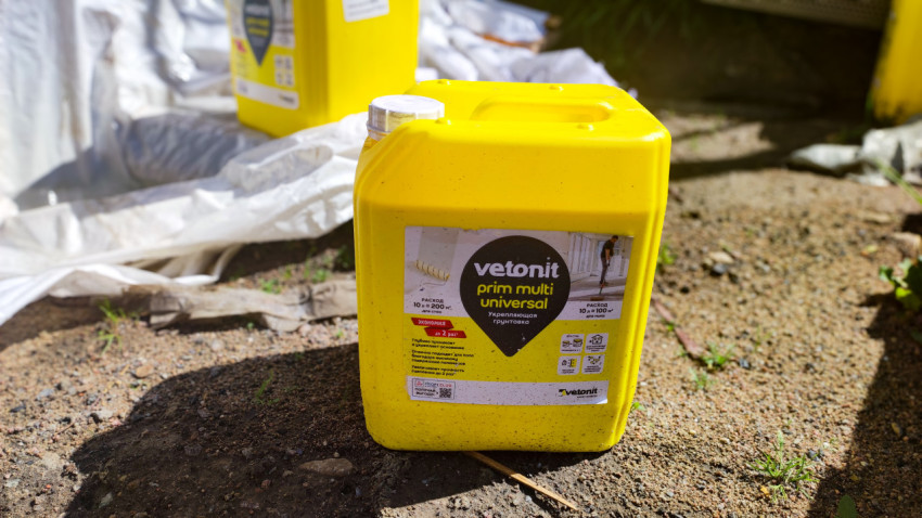 Жёлтая канистра грунтовки Vetonit на грунте возле укрывной плёнки