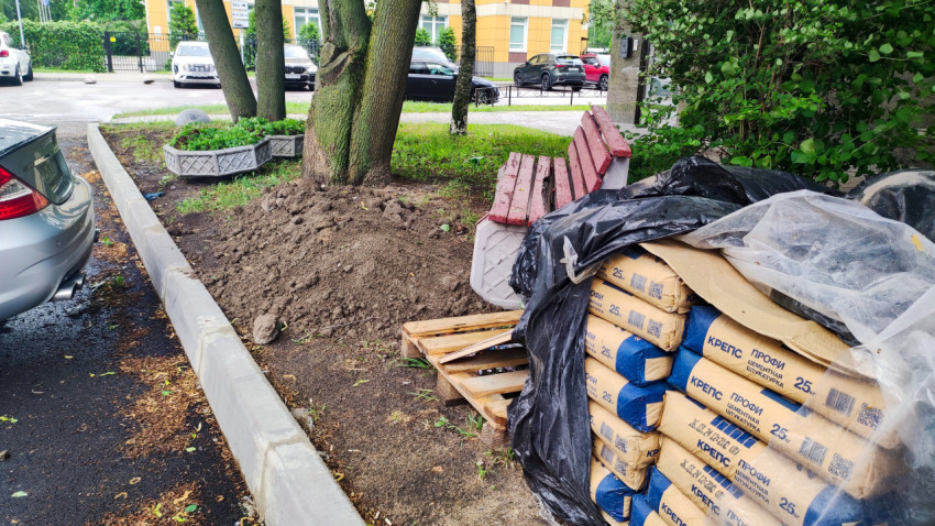 Стройматериалы в мешках, деревянные поддоны и куча грунта у деревьев во дворе