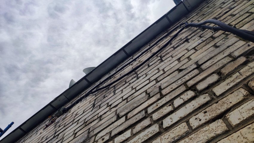 Верхняя часть кирпичного фасада с карнизом, кабелями и облачным небом