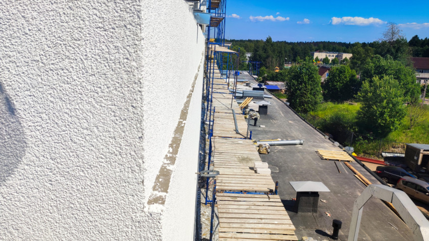 Фактура белой штукатурки и строительные леса вдоль стены над плоской кровлей с материалами и воздуховодами