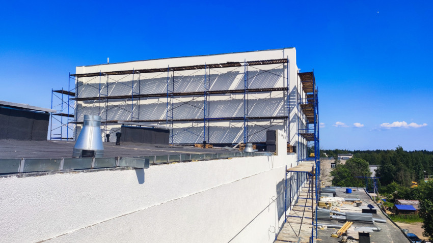 Плоская кровля с вентиляционными зонтами и строительными лесами у белого фасада в процессе ремонта