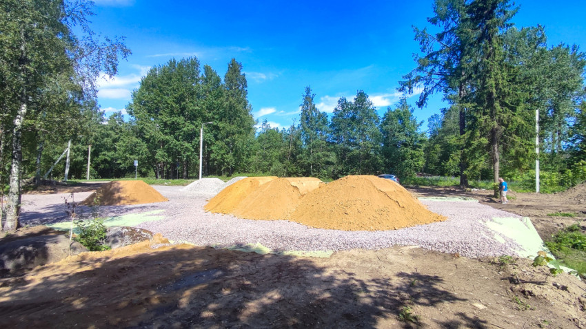 Складирование песка на щебёночной площадке с деревьями и человеком у края работ
