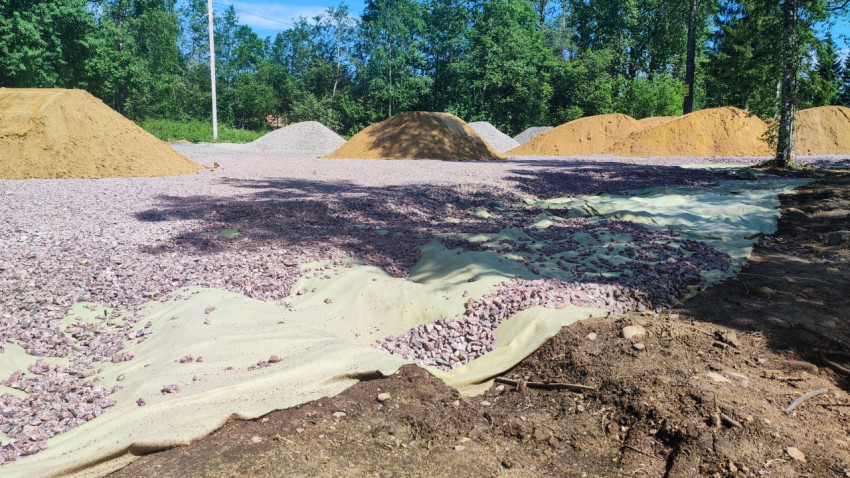 Зелёный геотекстиль с насыпанным щебнем и кучами песка на площадке у леса