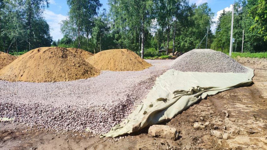 Кучи песка и щебня на геотекстиле на фоне берёз и леса