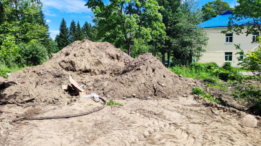 Кучи вынутого грунта рядом со зданием с синей крышей на фоне леса