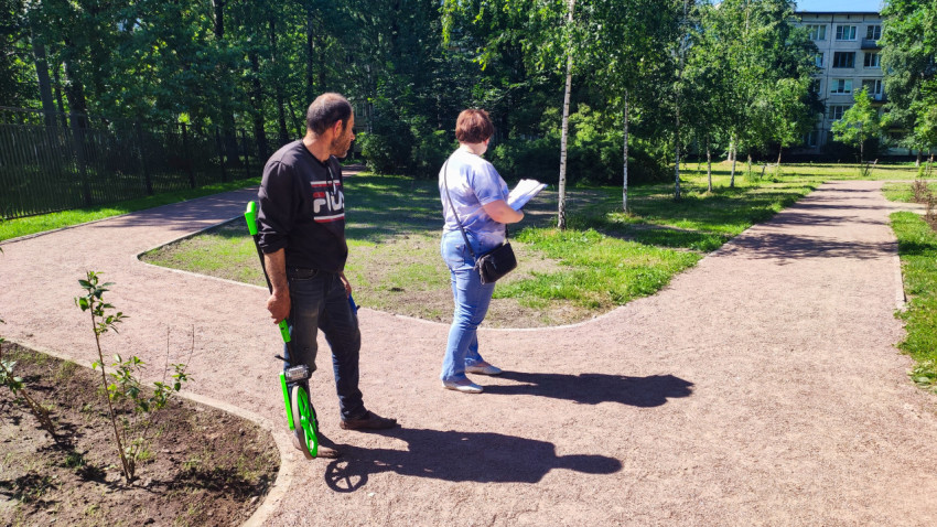 Рабочий с измерительным колесом и женщина с документами стоят на изогнутой пешеходной дорожке в сквере