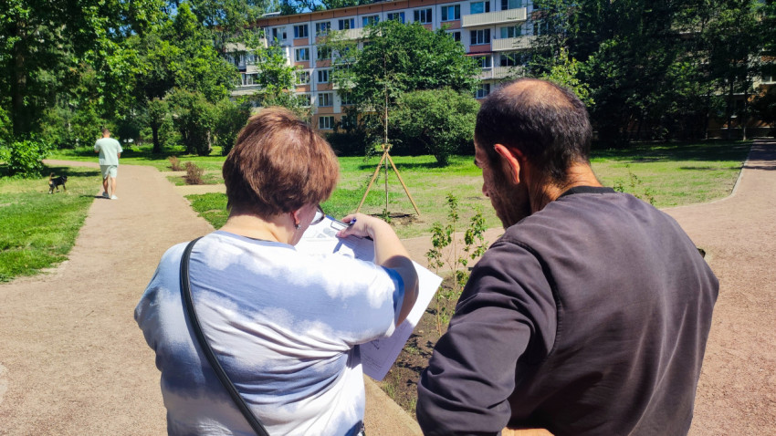 Женщина показывает документы мужчине на фоне дворовых дорожек и жилого дома