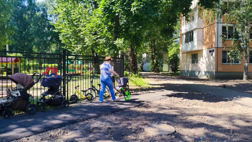Женщина катит измерительное колесо по дворовой дорожке у ограждённой детской площадки