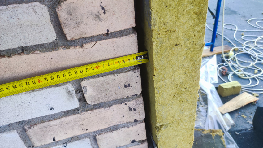 Замер рулеткой зазора между кирпичной кладкой и плитой минеральной ваты на крыше