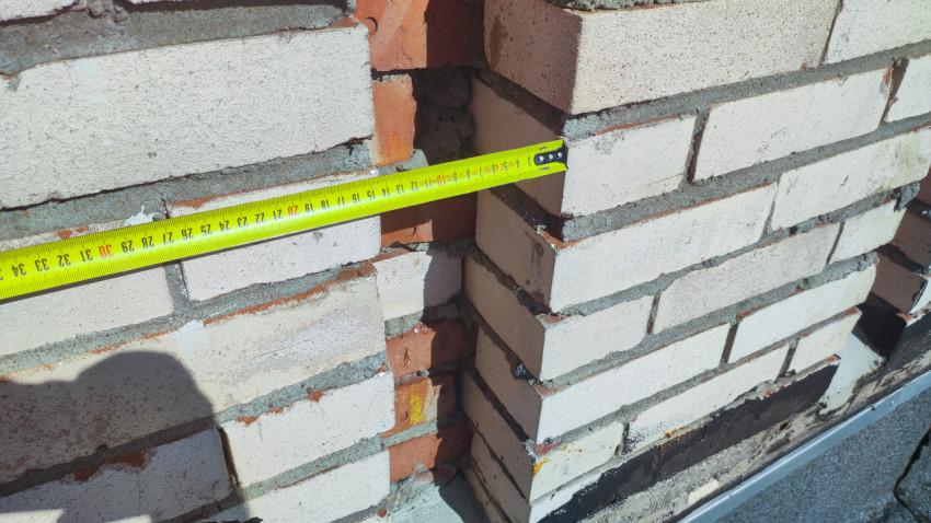 Диагональный замер рулеткой ширины кирпичного проёма у гидроизоляции парапета