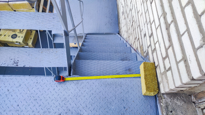 Рулетка и минераловатный утеплитель на металлической лестнице плоской кровли
