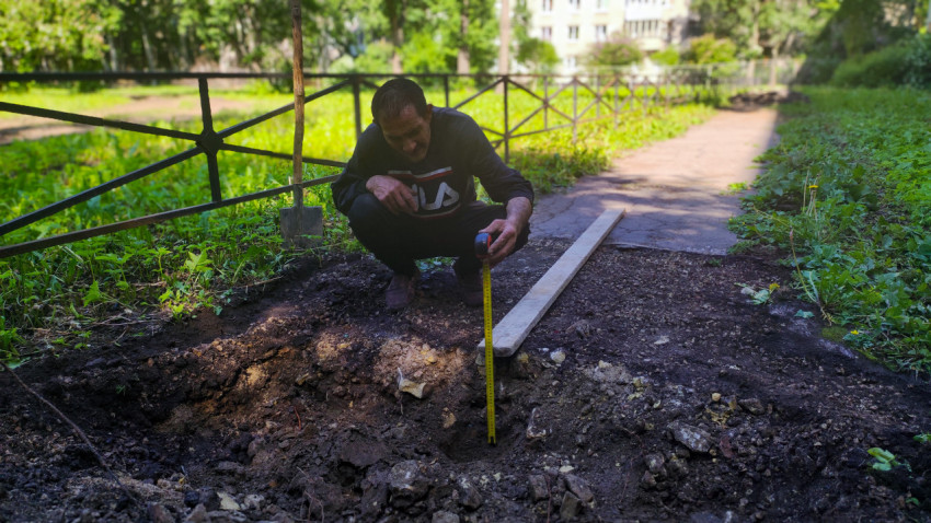 Рабочий измеряет глубину раскопа рулеткой на дворовой дорожке