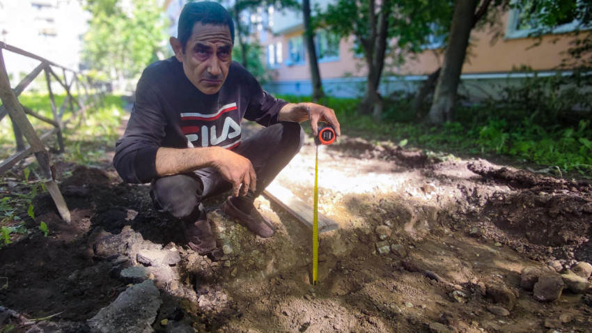 Рабочий с рулеткой у раскопа на дворовой дорожке