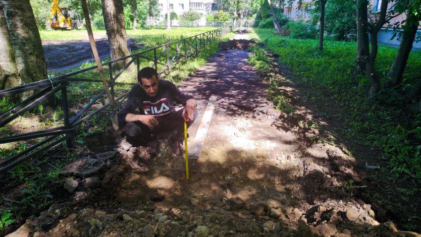 Рабочий с рулеткой у выемки на дорожке и лопата у ограждения