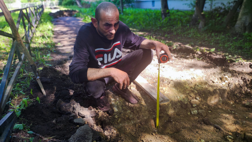 Замер глубины раскопа рулеткой на участке ремонта дорожки