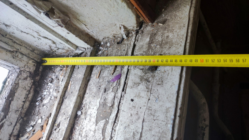 Рулетка измеряет ширину повреждённого деревянного порога у оконного проёма