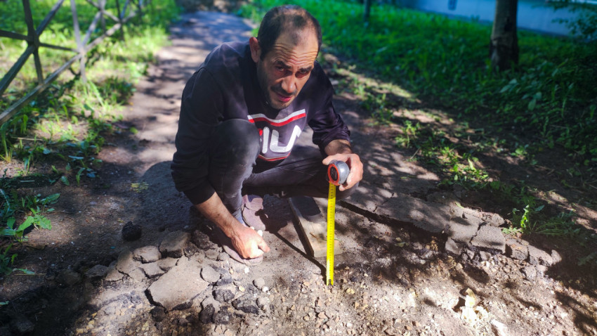 Мужчина с рулеткой измеряет глубину раскопа на пешеходной дорожке