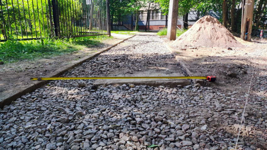 Измерение ширины дорожки с щебнем рулеткой рядом с кучей песка