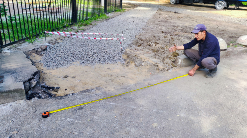 Мужчина с рулеткой измеряет участок разрушенного асфальта рядом с засыпанной щебнем траншеей