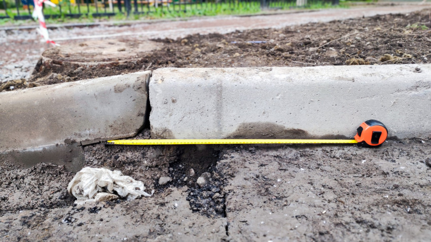 Измерение рулеткой длины бордюрного камня с заметным зазором между секциями