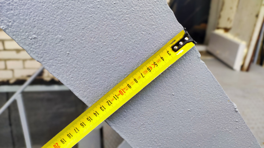 Рулетка измеряет ширину серой металлической балки у входа в здание