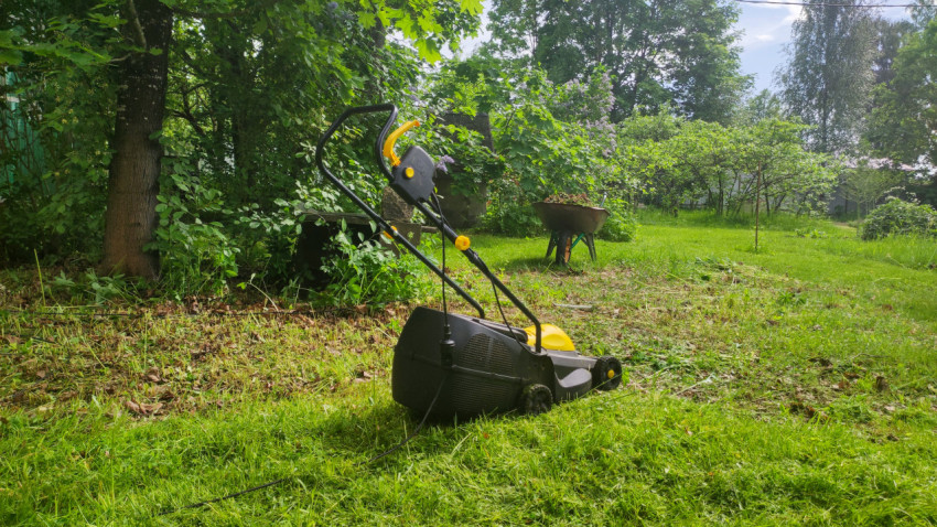 Электрическая газонокосилка с кабелем на газоне приусадебного участка
