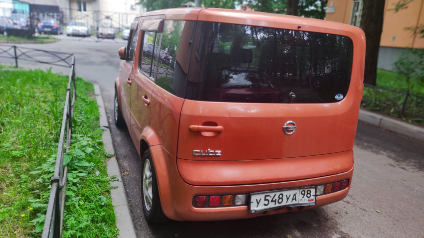 Задняя часть оранжевого Nissan Cube на дворовой парковке
