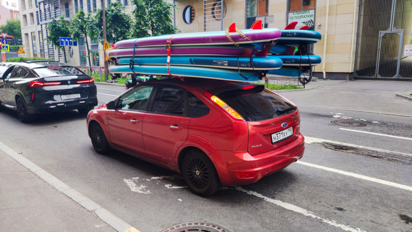 Ford Focus перевозит несколько надувных SUP-досок на крыше на фоне городской застройки и дорожных знаков