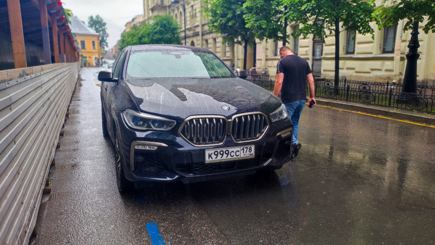 BMW на мокрой улице рядом со строительным ограждением и пешеходом в городской застройке