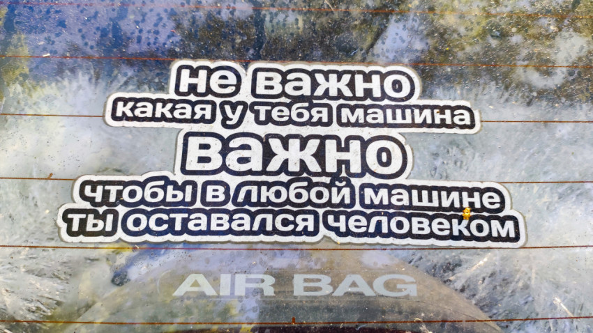 Наклейка с текстом «Не важно какая у тебя машина…» на запылённом стекле автомобиля с надписью AIR BAG