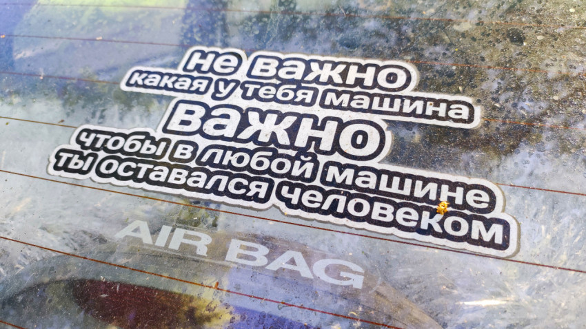 Наклейка с фразой о культуре вождения на пыльном стекле автомобиля, снятая под углом