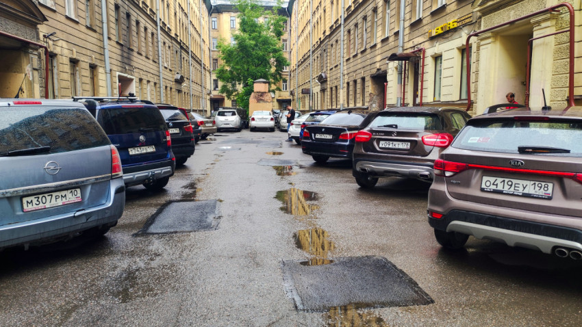 Двор-колодец с припаркованными машинами и лужами между фасадами старых домов