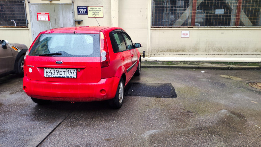 Красный Ford Fiesta на мокрой парковке у здания с табличками «Котельная» и «Проход запрещен»