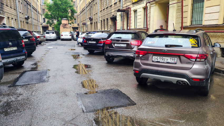 Дворовая парковка после дождя с автомобилями и лужами у фасадов жилых домов