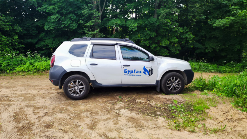 Белый служебный кроссовер с логотипом «БурГаз» на грунтовой дороге у леса