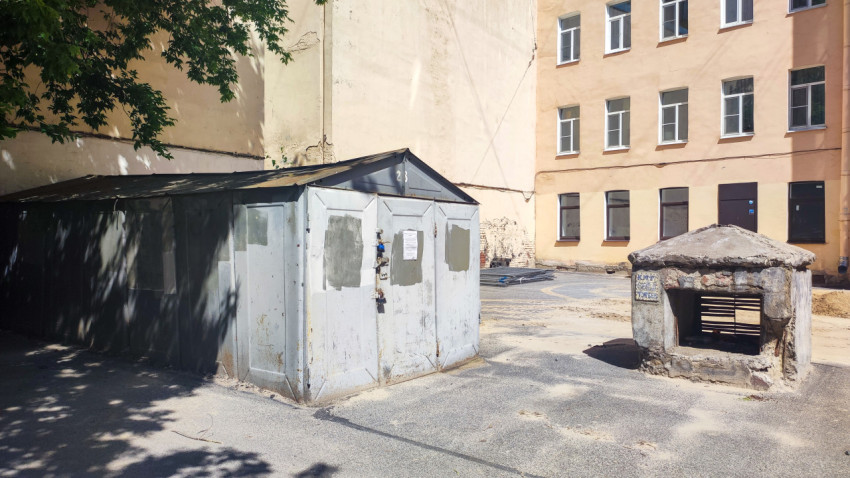 Металлический гараж во дворе рядом с вентиляционным выходом подвала и фасадом здания