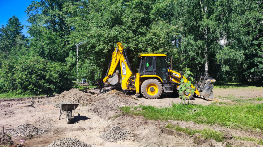 Экскаватор-погрузчик JCB выполняет земляные работы на площадке у лесополосы