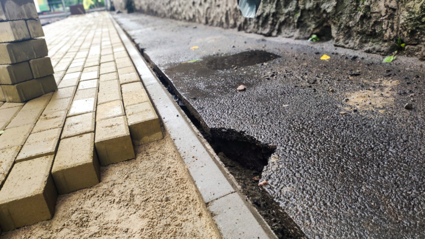 Провалившийся участок асфальта вдоль бордюра рядом с укладкой тротуарной плитки