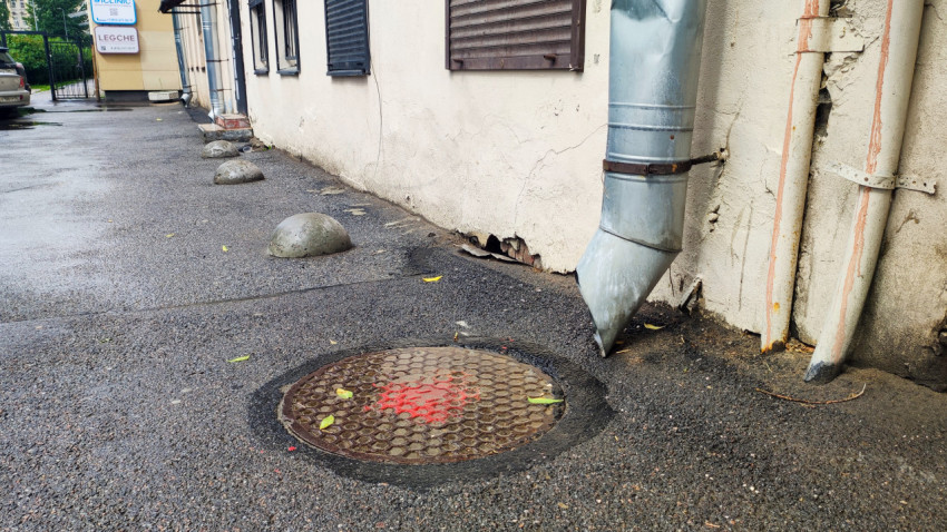 Водосток и инженерные трубы у люка во дворе на фоне изношенного фасада