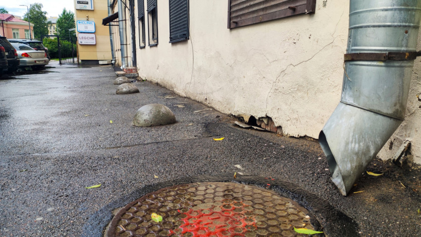 Люк с красной разметкой и водосточная труба у треснувшего цоколя здания