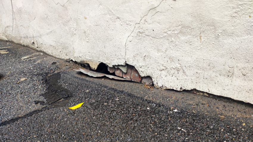 Отверстие в разрушенном цоколе с оголённой кирпичной кладкой у мокрого асфальта