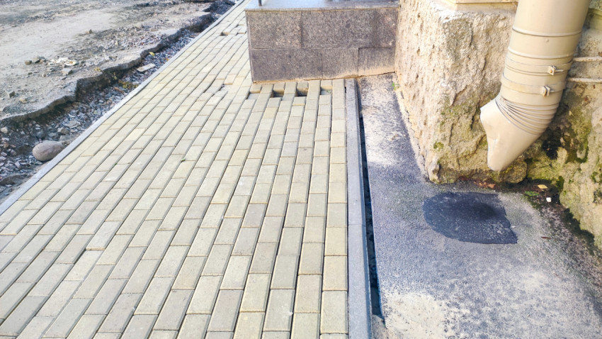 Дефект мощения у угла здания рядом с водосточной трубой