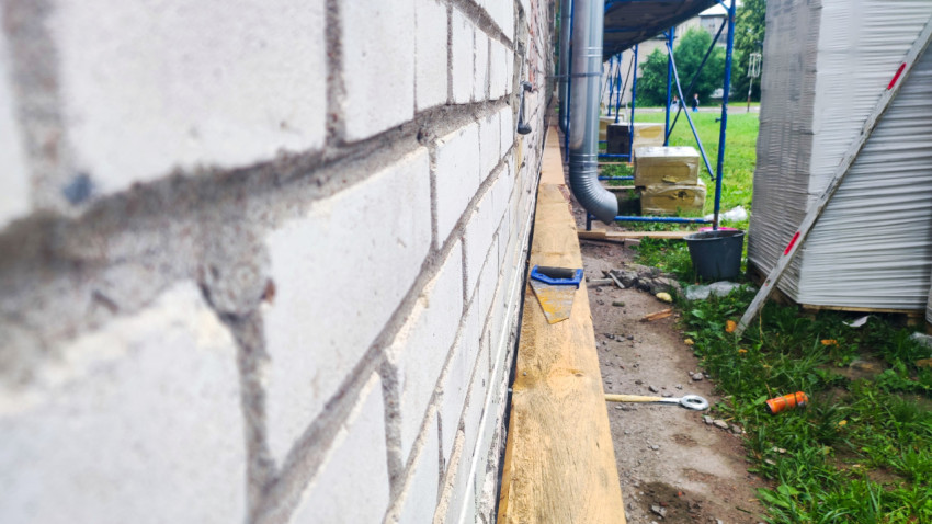 Кирпичная стена вдоль строительных лесов с инструментами у фундамента