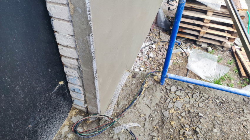 Угол фасада с армирующей сеткой и проводами у основания на стройплощадке